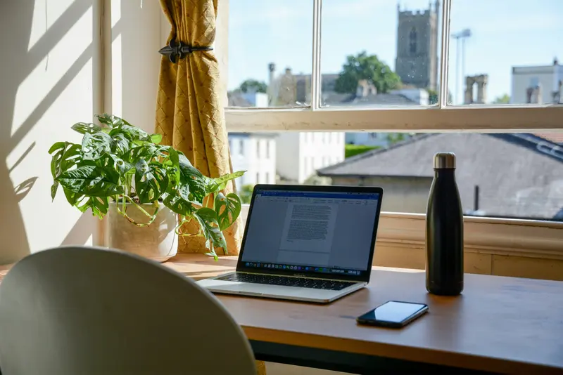 Home office organizado com notebook sobre a mesa, junto à janela